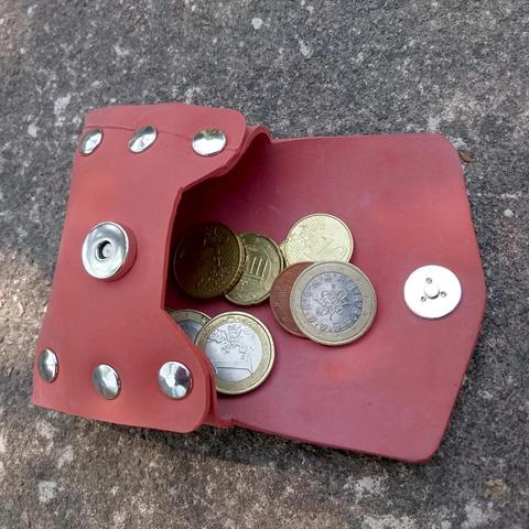 Un des porte-monnaie en chambre à air rouge, à la lumière du soleil, ouvert, avec de la monnaie à l'intérieur