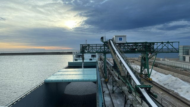 A ship's cargo hold being loaded with road salt by a conveyor belt. Seen from the bridge.
