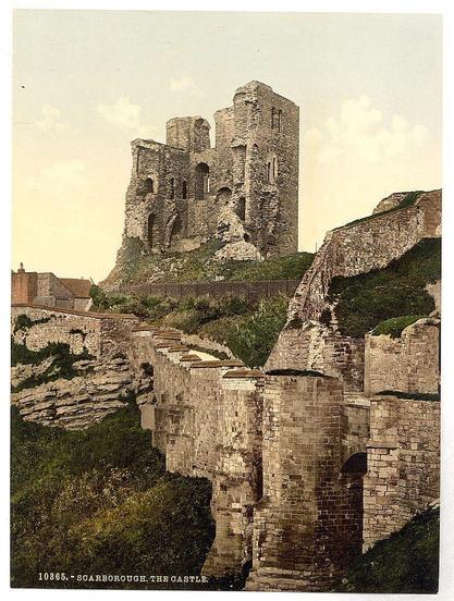 The image depicts the ruins of a historic castle known as Scarboro, located in Yorkshire, England. The photograph captures an expansive view showcasing multiple stone walls and towers that are eroded by time. These remnants rise against a backdrop with patches of greenery, indicative of vegetation growth within or around these old fortifications. In the foreground to the left, modest structures appear partially hidden amidst tall grasses, possibly suggesting nearby residential buildings or other small establishments.

A prominent feature is the fortified tower (keep) at the center-right portion of the image which stands as a testament to past architectural prowess and defense mechanisms commonly found in medieval castles designed for both habitation and military purposes. The stone walls are seen crumbling on some sections, revealing how they once stood tall with purposeful design, possibly housing living quarters above ground level.

The sky is partly cloudy but allows sunlight to filter through, casting a warm glow across the landscape and creating an ethereal atmosphere that adds character to this historical ruinous site. Overall, it's a snapshot of British heritage captured in its faded grandeur during late 19th or early 20th-century photography techniques, as indicated by the print number (10365) at the bottom left corner.