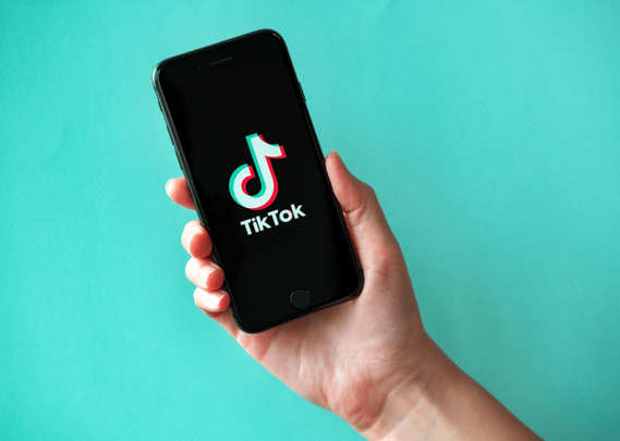 Un utilisateur tenant un smartphone avec le logo TikTok affiché sur l'écran, sur un fond turquoise.
