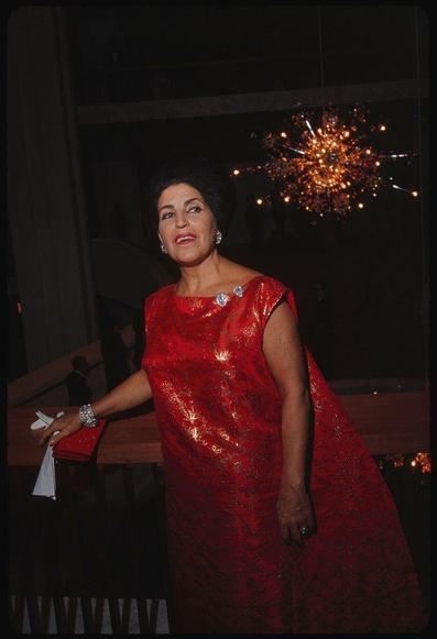 woman in red sequined dress and sparklers at back of head, with her hand on the table.