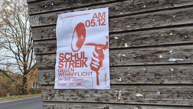Weißer Plakat mit rotem Aufdruck "SCHULSTREIK" und Datum "05" sowie einem stilisierten Piktogramm einer Person mit erhobener Faust, angebracht an einer Holzfassade.