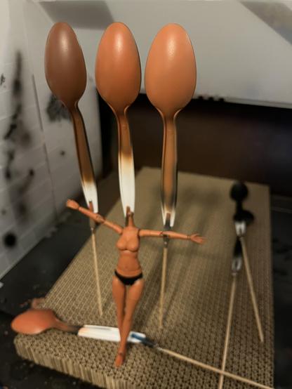 Three plastic spoons in a portable spray box painted with different shades of brown to replicate some darker skin tones. Below them is an assembled model kit using the middle mixture.