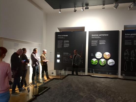 Blick in den Raum des Steiermark Reliefs im Naturkundemuseum Graz, Wolfgang Paill (Leiter), spricht vor bedruckten Paneelen zu den Gästen.