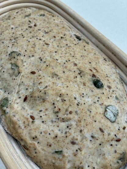 Seeded sourdough in a batard banneton showing seeds, sage and seaweed on the surface.