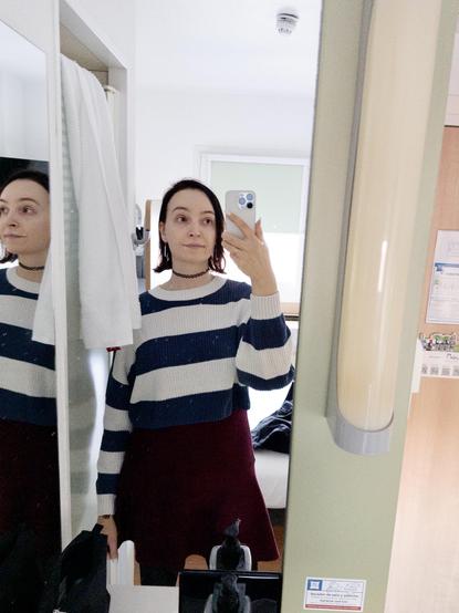 Me in a hotel room mirror, I’m wearing a white and navy blue striped sweater and a wine red skater skirt