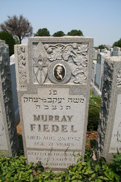 photo of a gravestone in a densely packed Jewish cemetery. this is of Murray Fiedel, died Aug 25 1952. there's an inset photo of him wearing a bowtie in the ornately carved upper part of the gravestone.