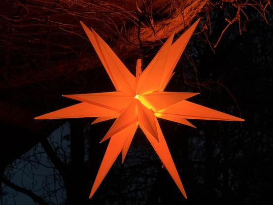 Orange leuchtender Stern im Stil eines Herrnhuter Sterns in der Dunkelheit