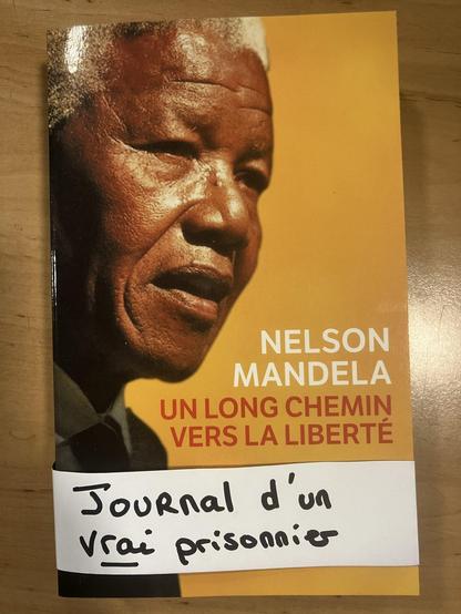 Posé sur une table en bois, le livre de Nelson Mandela : Un long chemin vers la liberté.
Une note sur le livre écrite à la main : Journal d'un vrai prisonnier