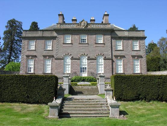 The House of Dun near Montrose in Angus. The image shows the grey stone house standing beyond its garden and steps. It is seven bays wide and two storeys high with an ornate roofline and four blocks of chimneys. A well-manicured hedge cuts across the frame this side of the house. The sky is blue.