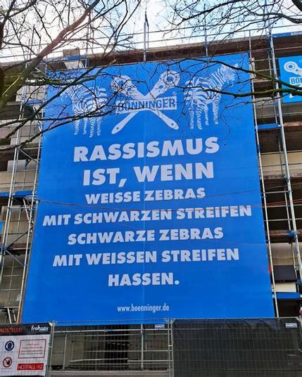 Großes, blaues Plakat an Gerüst: Rassismus ist, wenn weisse Zebras mit schwarzen Streifen schwarze Zebras mit weissen Streifen hassen. www.boenninger.de