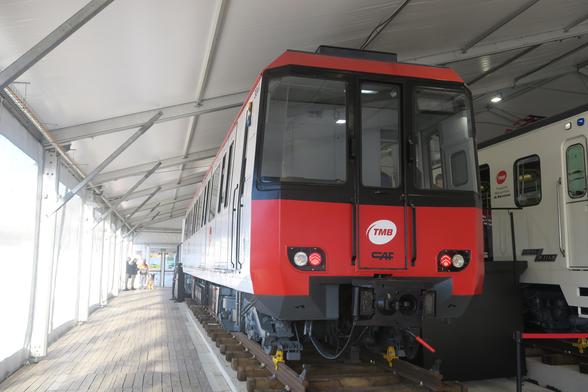 Unitat de la sèrie 3000 del Metro de Barcelona. És un tren de laterals blancs i frontal vermell amb tocs negres, dels anys 80, exposat sobre un pedestal en una carpa al carrer.