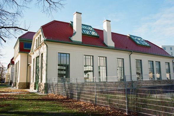 Diesmal sieht man in die östliche Seite der alten Hauptwerkstatt in voller Breite und nach hinten hin verlaufend sogar das gesamte Ensemble vom alten Verwaltungsgebäude weg entlang der Marischkapromenade. (Die Promenade ist sehr fein, aber natürlich verhindern die Bäume größere Bilder von der Fassade.) Die besondere Attraktion der neu renovierten Gemeinschaftswerkstatt sind die sehr hohen Räume im Erdgeschoß und die eindrücklichen Lichtblenden auf dem Dach des Gebäudes. Auch die Kamine wurden originalgetreu renoviert, wie hier schön zu sehen ist. Ich freue mich jetzt schon darauf, wenn die Ateliers und Werkstätten mit Leben gefüllt werden.