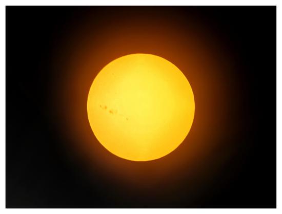 Photo of the sun with sunspots, edited to be a yellow disk surrounded by a reddish glow against a black background. The sunspots are in a cluster on the left (western) side of the solar surface.

Taken with an iPhone 15 attached to a Celestron 130mm reflector telescope fitted with a solar filter. Edited in Snapseed.