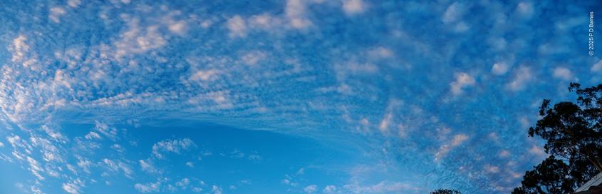 A broad sweep of sky covered in puffy white clouds, still dark to the north-west with occasional glimpses of white, through to bright in the south-east where the morning sun is lighting them brightly.