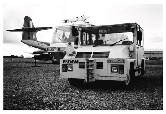 Black and white photograph of vintage airfield vehicles at Carlisle Aviation Museum.  To the left a jet, in the middle a fire tender, and to the right an aircraft tug.