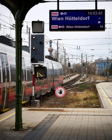 Ein Zug verlässt die Station, vor dem Zug ist ein Signal zu sehen welches 2 weiße Lampen untereinander zeigt, in der Ferne noch eines welches zwei grüne Lampen vertikal untereinander zeigt.