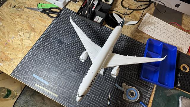 An overhead view of a white model airplane with Lufthansa branding, placed on a cutting mat.