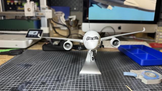 A model airplane is displayed on a stand in front of a computer monitor.