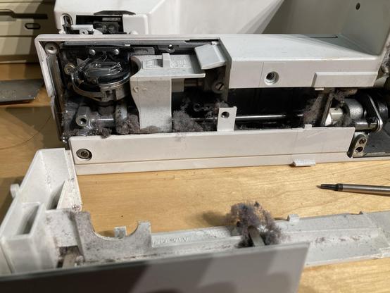 The guts of the underside of a sewing maching. It has a long crankshaft that connects to a bobbin. The bobbin and its gears are packed with dust and lint.