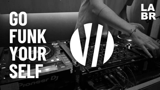 Black & White Photo. Witton over a Pioneer DJ System set up. Right hand on left deck. Bracelet on wrist of right hand. Short sleeved shirt. In white letters, his show title. Go Funk Yourself. Upper right hand side is the LABR logo in white blocked letters. LA on top BR on the bottom.