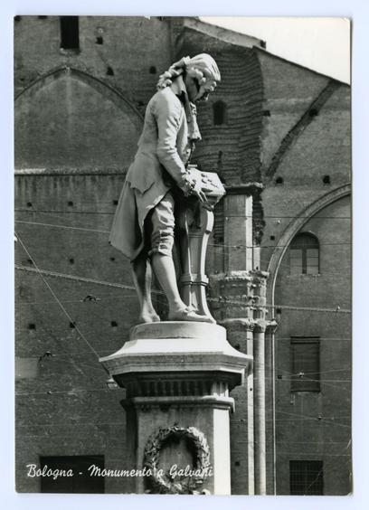 The black and white photograph displays an antique statue in Bologna, prominently labeled as the "Monumento a Galvani." The sculpture is dedicated to Luigi Galvani, a renowned Italian physicist known for his pioneering work on electricity and animal life. In the image, we see two figures: one appears to be Galvani himself, clad in period clothing that includes breeches, stockings, and shoes indicative of 18th-century fashion. He stands upright with an air of dignity, suggesting a commemoration of scientific achievement.

The second figure is likely representing a dissected frog or another animal specimen, which was often used by Galvani to demonstrate his electrical experiments on lifeless bodies. The positioning suggests that the statue captures one of Galvani's famous electro-muscular stimulation demonstrations where he reanimated dead flesh through electric current.

The base of the sculpture is adorned with a wreath and bears an inscription "Compianto 1793," which translates to "Complaint" or possibly indicates mourning, potentially referencing a particular incident in Galvani’s life. The background reveals part of Bologna's historic architecture, including what looks like Romanesque arches and brickwork typical of the city.

Overall, this statue stands as both a tribute to Galvani’s scientific legacy and an artistic representation capturing his innovative work on electricity and its effects on living organisms during the Enlightenment era.