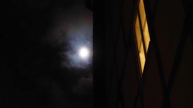 Mond an wolkigem Nachthimmel aus einer Gasse betrachtet, Fenster  sind erleuchtet
