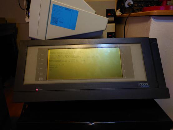 A picture of the Apricot portable sat on top of a cabinet, showing the old greyscale wide aspect LCD showing the DOS prompt.