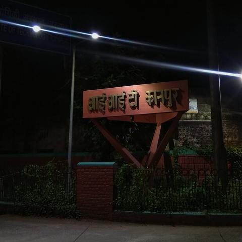 A night scene with a sign reading "IIT Kanpur" in Hindi, illuminated by streetlights. (colored)