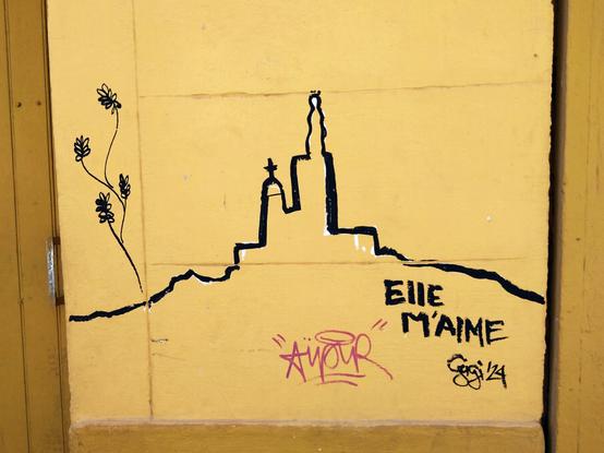 A black line depicting Marseille's Notre Dame de la Garde on a yellow wall, with the caption "Elle m'aime" (she likes me).