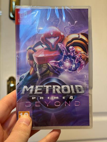 My freshly delivered copy of Metroid Prime 4 Beyond. Samus, a female bounty hunter in a sci fi space suit, is reaching out towards the camera. Behind her, several alien robots are lurking.