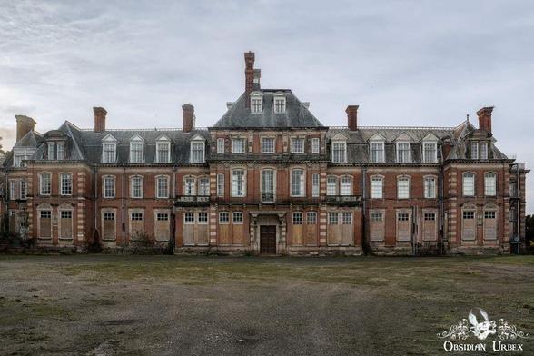 A large, abandoned, three-story brick mansion with boarded-up windows and a neglected yard under a cloudy sky.