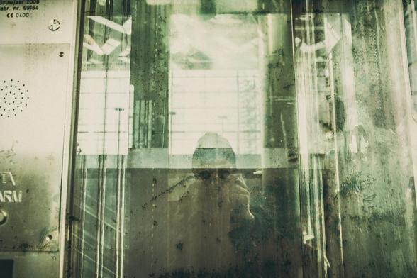 personne aux lunettes noires se prenant en photo devant un miroir, fondé enchaîné sur une structure de verre et de métal peu identifiée