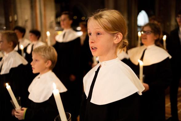 Kinder in weißen Gewändern mit Kerzen in den Händen, vermutlich bei einer religiösen Zeremonie in einem dunklen Raum.