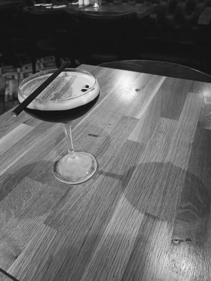 Espresso martini on a wooden table with shadow.