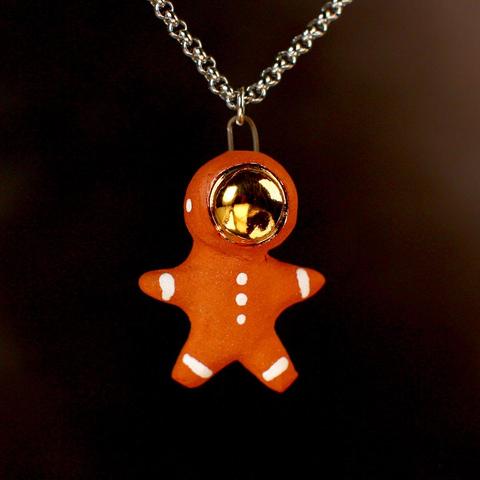 A gold masked ceramic astronaut pendant in terra cotta made to look like it is made of gingerbread with little white frosting details.