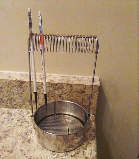 a metal brush-holder rack with a wire coil that a couple of narrow-handle paintbrushes are wedged into