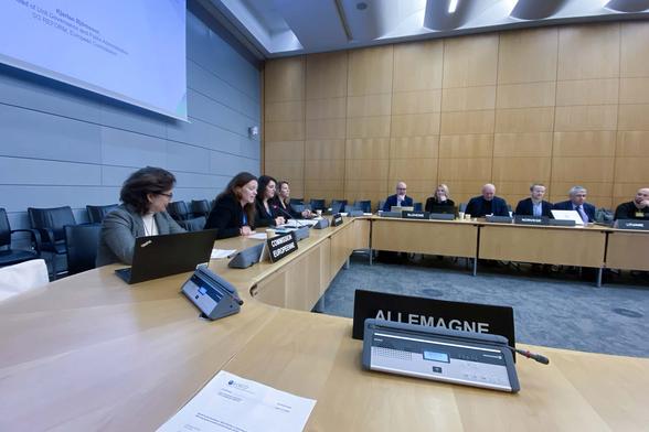 A formal table setting with people sitting in a large conference room, signs in front of people say European Commission, Slovenia, Lituania, Norway, and Germany