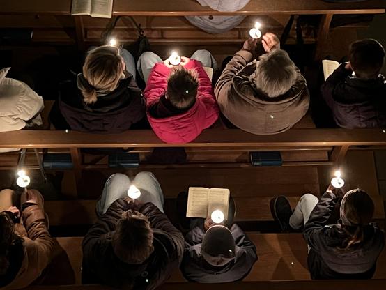 Gottesdienst-Mitfeiernde mit Kerzen in der Hand von oben fotografiert.