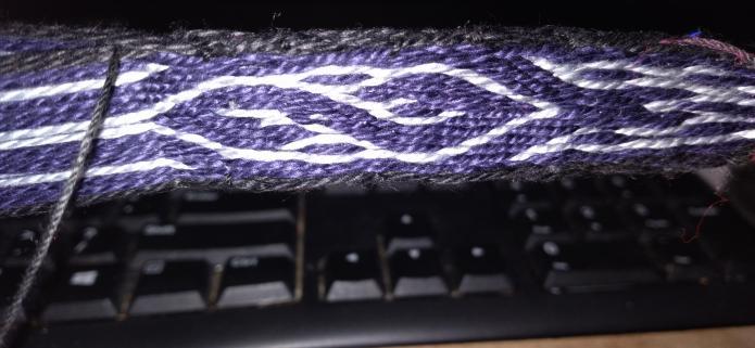 Close up of in-progress tablet weaving, dark purple with grey design and black borders