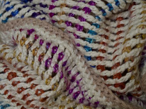 Closeup of a hand-knit afghan consisting of alternating rows of white and multicolored yarn.