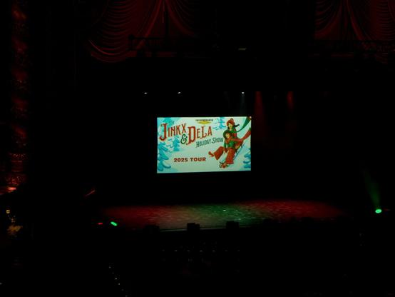 Photo of the stage at the Kings Theater in Brooklyn. The screen on stage shows the banner for the 2025 Jinkx & DeLa Holiday Show.