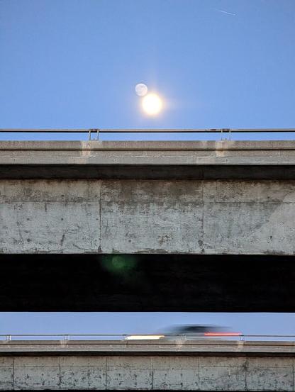 The moon over an overpass with a car driving by