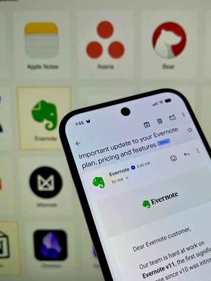 An Android phone showing Evernote's e-mail annoucing the rate increase, with the noteapps.info comparison page visible on a display in the background.