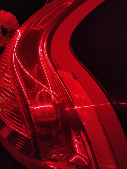 Close-up image shows the subtle, swooping curves and brilliant red of a car's brake lights glowing in the dark of night