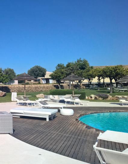 A tranquil poolside scene featuring lounge chairs, parasols, and a swimming pool surrounded by greenery and a stone wall under a clear blue sky.

Eine ruhige Landschaft am Pool mit Liegestühlen, Sonnenschirmen und einem Swimmingpool, umgeben von viel Grün und einer Steinmauer unter einem klaren blauen Himmel.