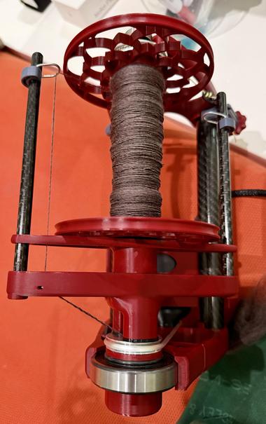 Espinner (cranberry colored) bobbin partially filled with singles in a brownish purple