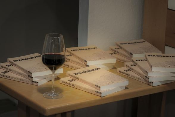 Der Büchertisch im Schriftstellerhaus Stuttgart, schlicht gehalten. Darauf mehrere Stapel mit dem neuen Roman "Der Mediator" von Moritz Hildt. Auf einer Ecke ein gefülltes Rotweinglas. Autorenherz, was willst du mehr!