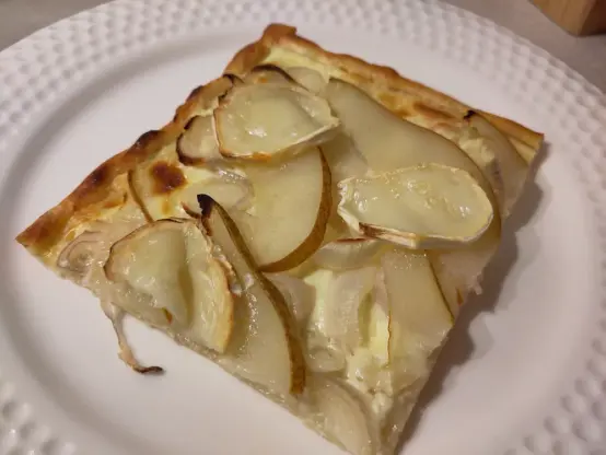 Ein Flammkuchen belegt mit Schalotten, Birnen und Ziegenweichkäse, der beim Backen geschmolzen ist.