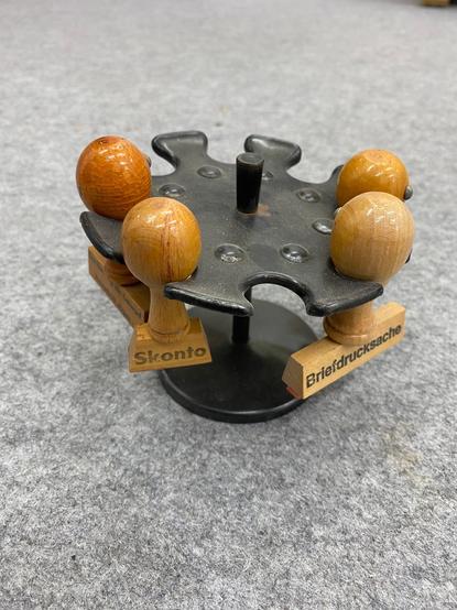Auf einem grauen Filz steht ein klassisches schwarzes Stempelrondell aus gepresstem Blech. In vier der acht Halterungen hängen Stempel. Auf zweien davon kann man eine Aufschrift sehen: "Skonto" und "Briefdrucksache".